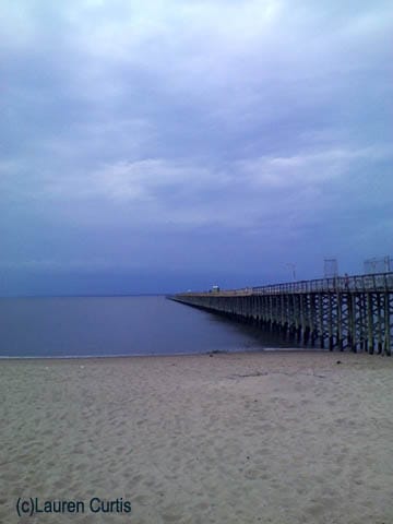 Keansburg Beach, New Jersey.  The sand meets calm waters of the ocean, blue sky with white clouds and a long pier going into the ocean.