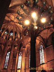 Photo of interior of Barcelona cathedral in Spain. ornate and historic, flying buttresses, stained glass windows, huge candelabras and glowing lights.