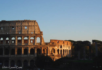 Color photo shot at sunset of the Colosseum in Rome, Italy.  Light casting shadows and a blue sky.