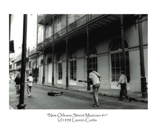 35mm black and white photo taken in the French Quarter in New Orleans, LA of a street musician playing guitar in front of an old building with elaborate wrought iron fences.