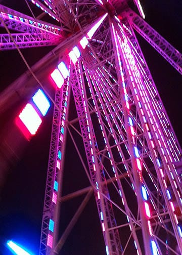 Close up of the center of a big Ferris wheel ride at night at a carnival. Red and blue lights.