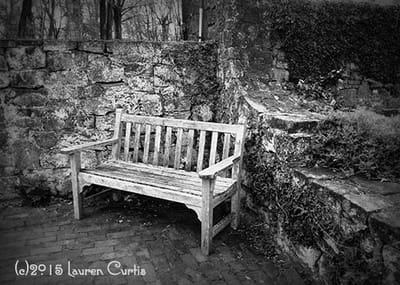 Black and white photo of an old wooden bench in front of a stone wall at Cross Keys Estate in New Jersey.