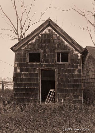 Sepia toned photograph of an historic, abandoned farmhouse barn. Open windows and door look like a creepy face. Somerset County, NJ.